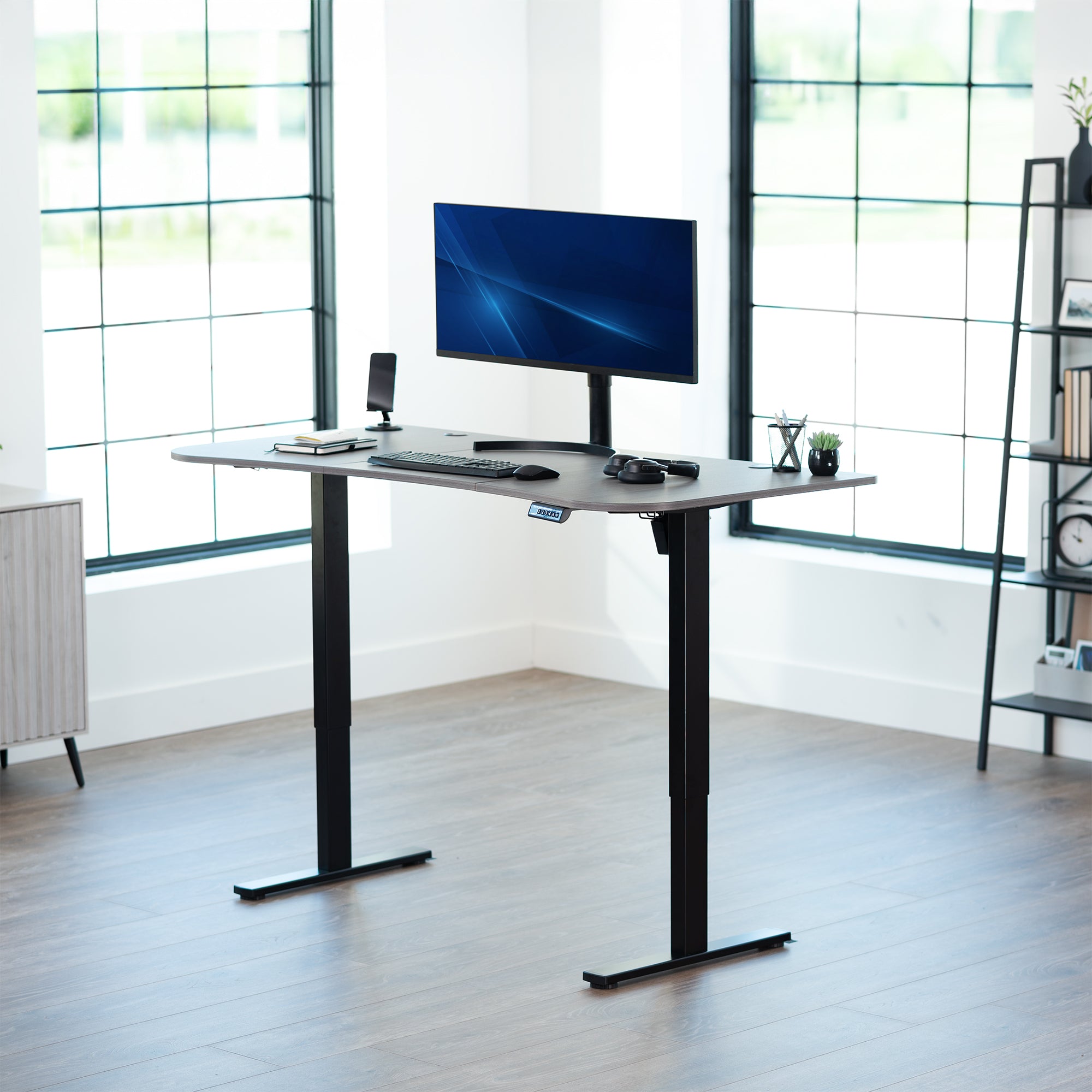 Grey, electric, sit to stand, height adjustable desk in office setting.