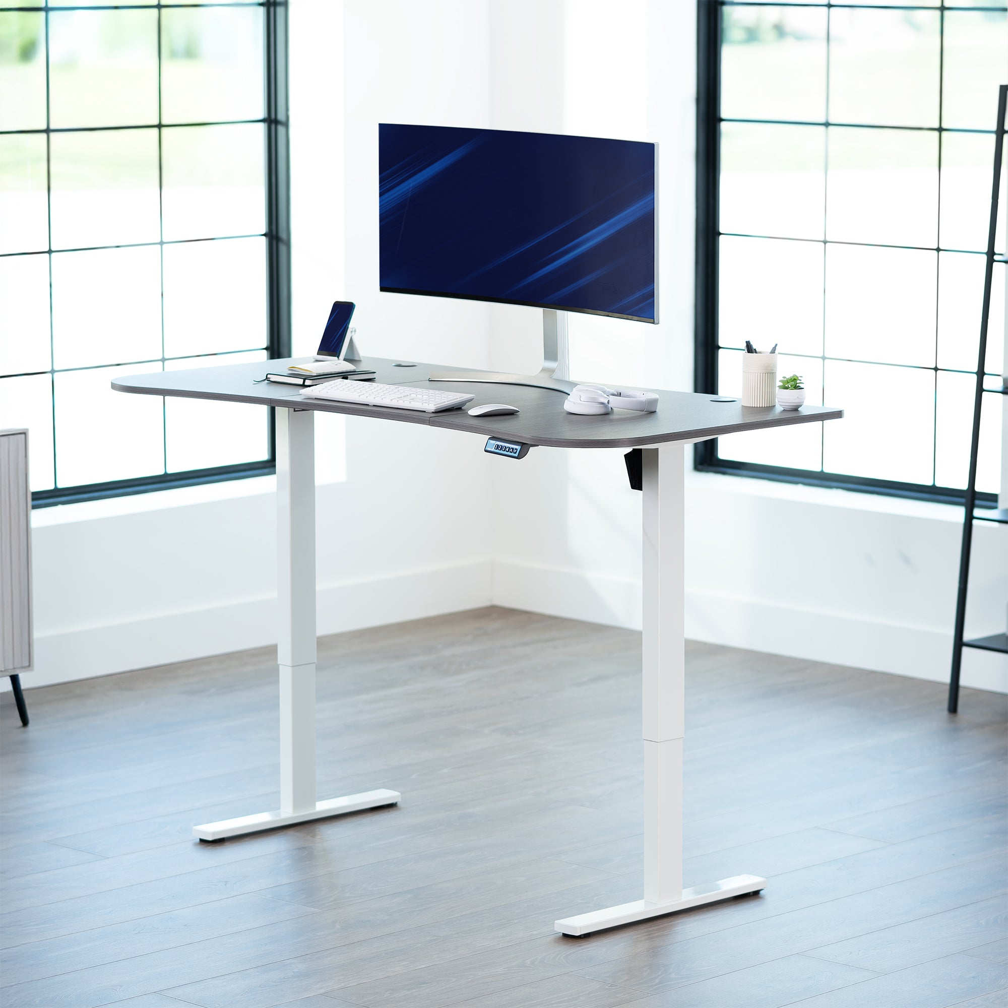 Dark grey top white frame, electric, sit to stand, height adjustable desk in office setting.