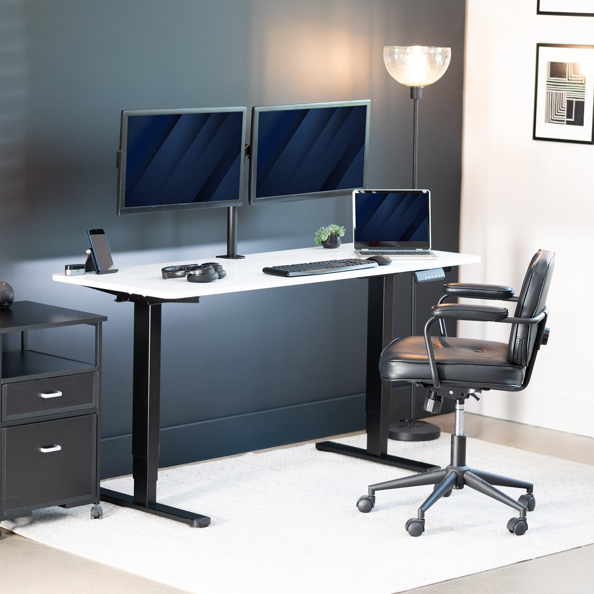 Modern office desk setup with two monitors, a laptop, and a chair in a well-lit room.