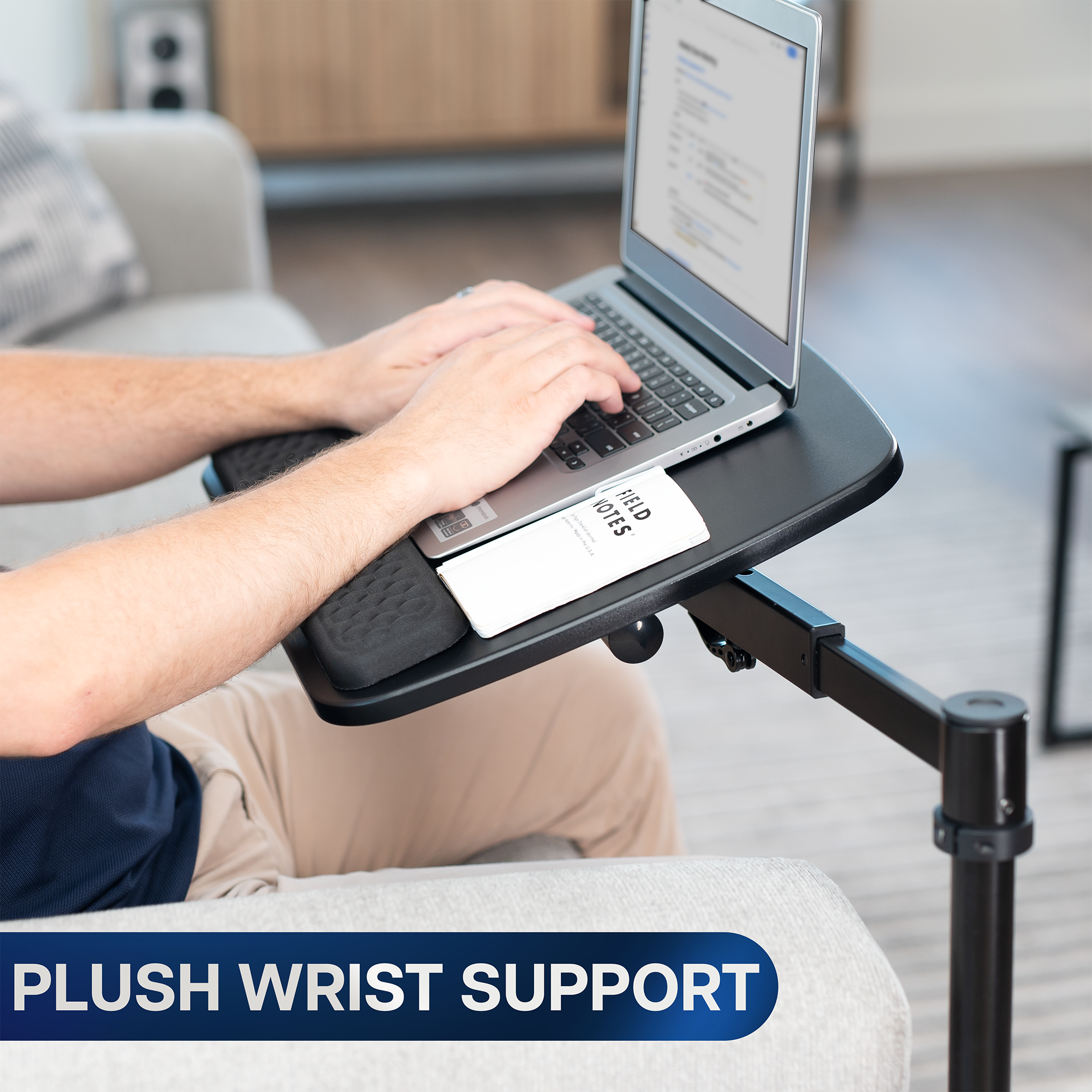 Person using a laptop on a adjustable tray with plush wrist support in a home setting.