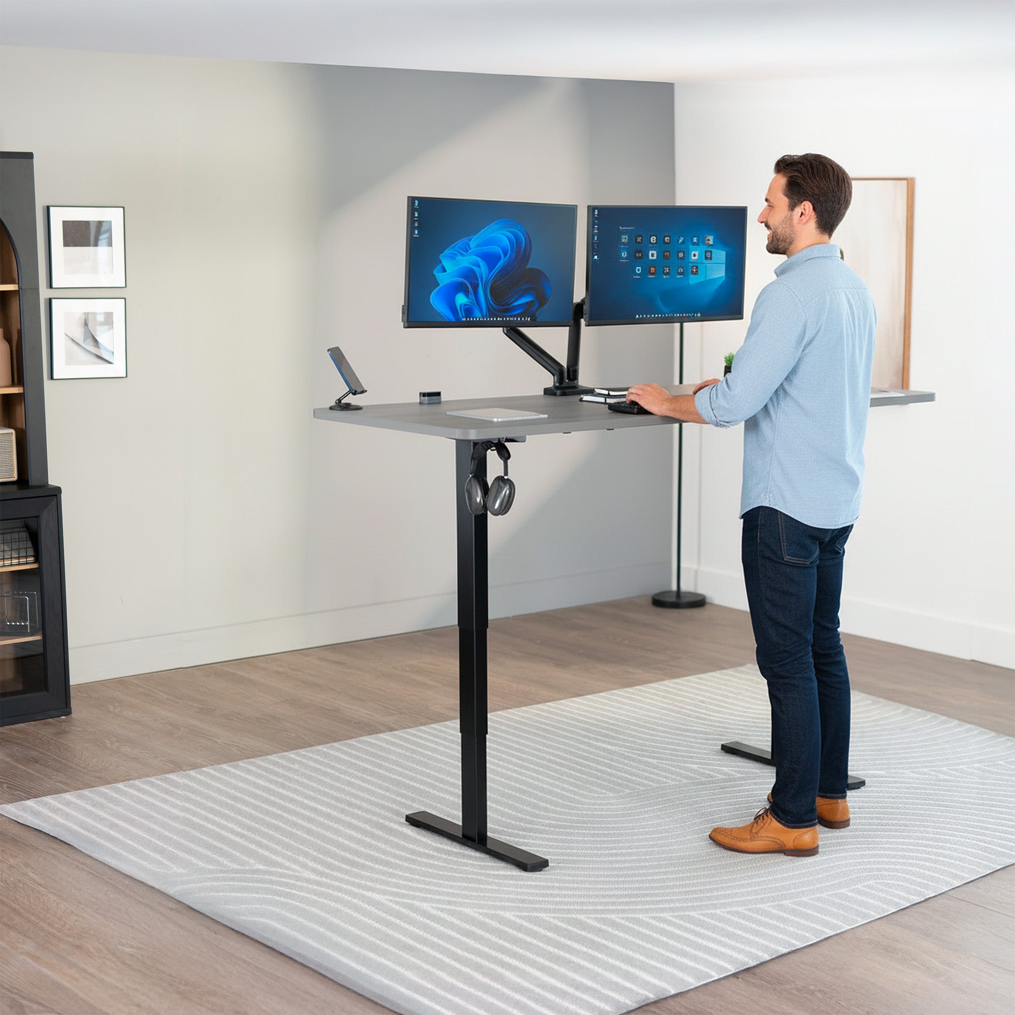 Person using a standing desk with dual monitors in a home office setting