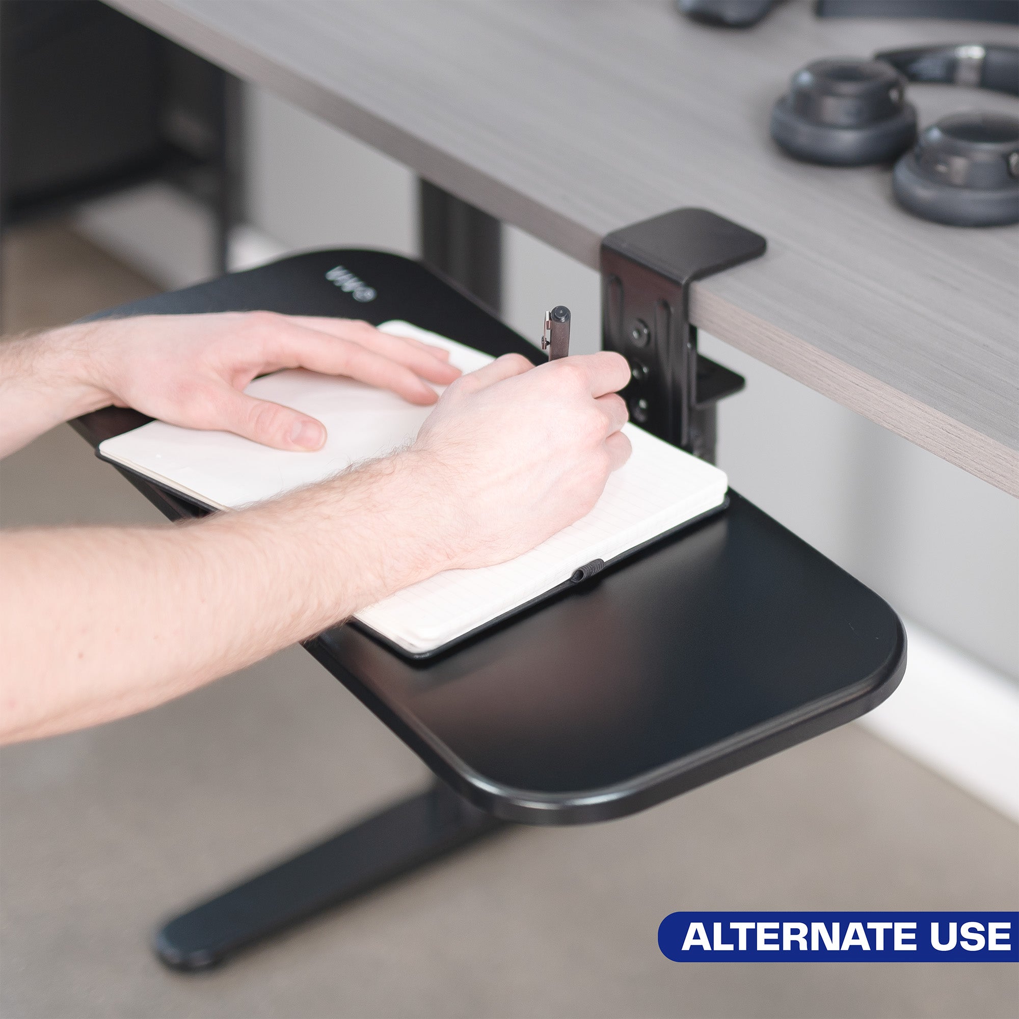 Single Clamp Rotating Keyboard Tray being used as an extension of the desk by a man writing in a notebook.