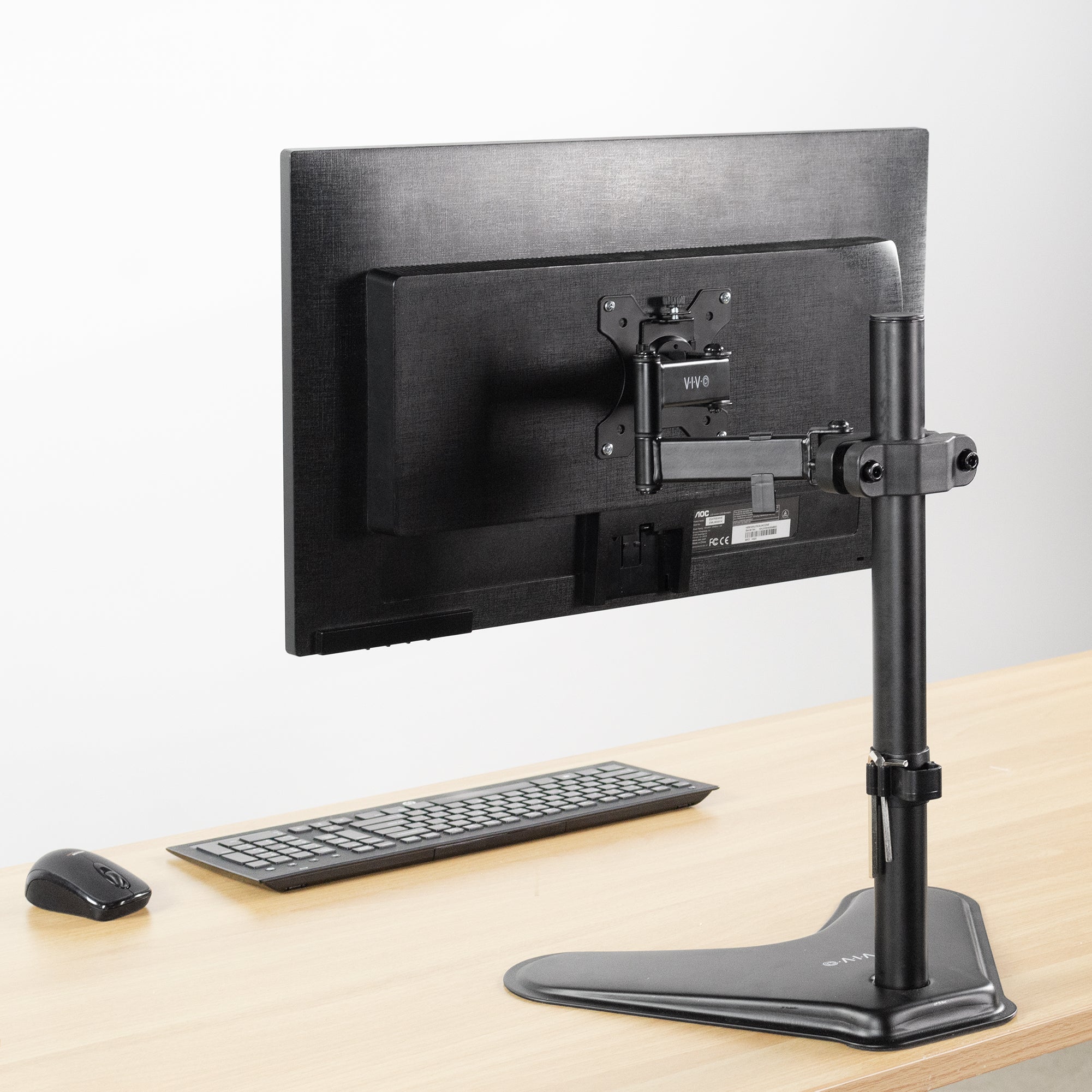 Pole Mount VESA Monitor Arm shown from the back on a light wood desk with a keyboard and mouse against a white background.