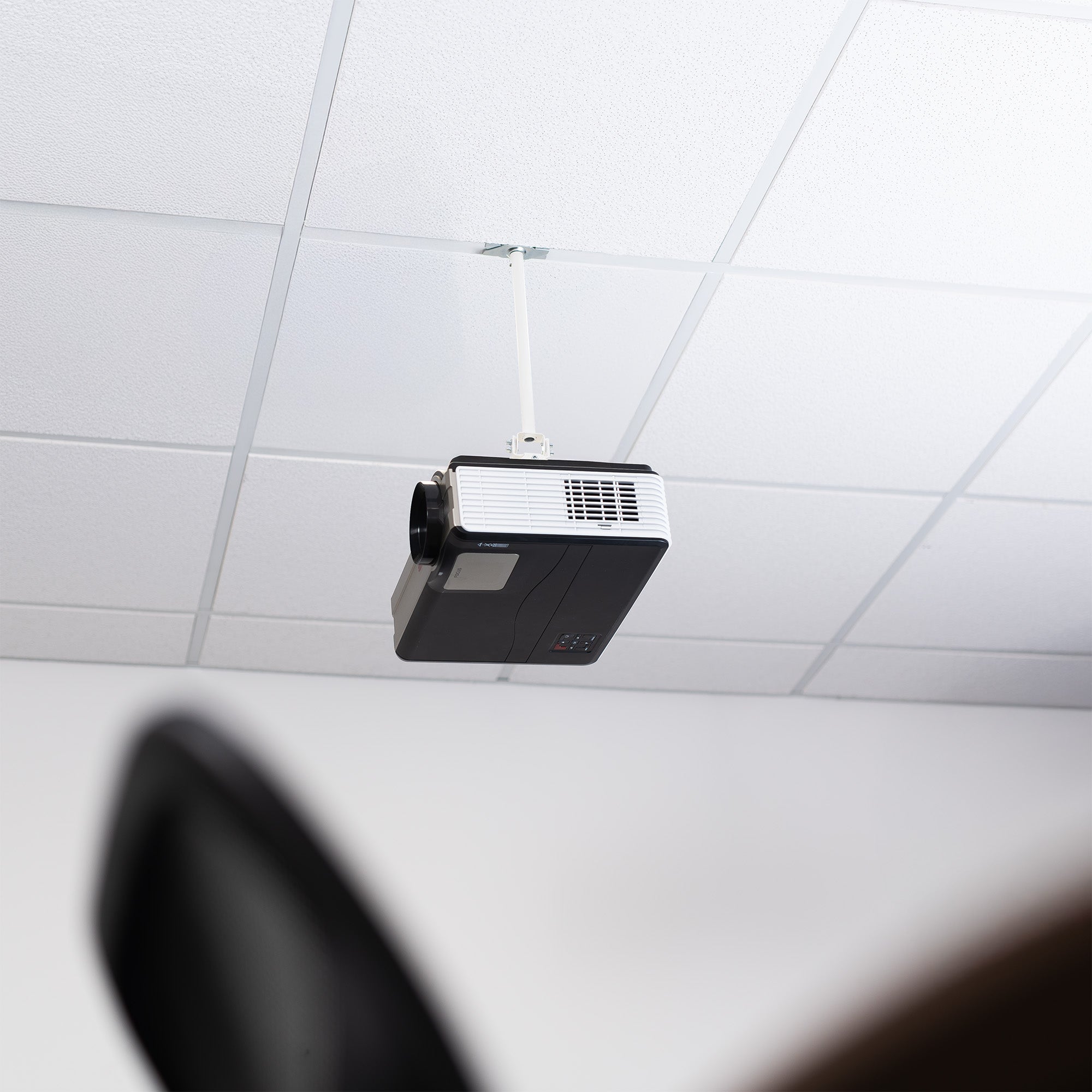 A white ceiling mount with scissor clamp designed to support projectors, featuring an adjustable length arm and a circular base.