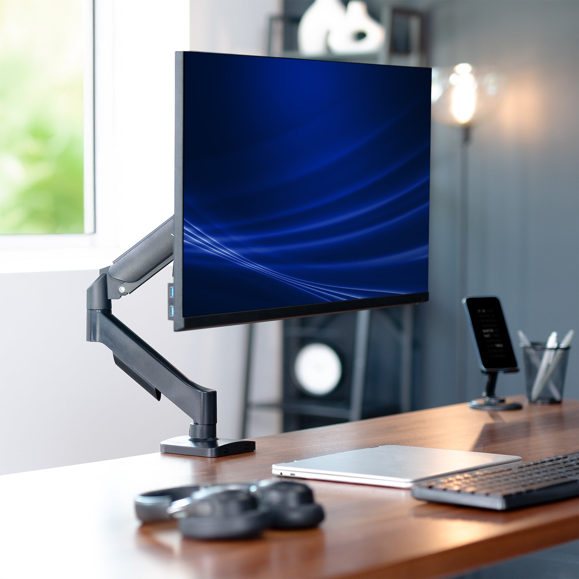 Computer monitor on a mechanical monitor desk mount with a blurred office background
