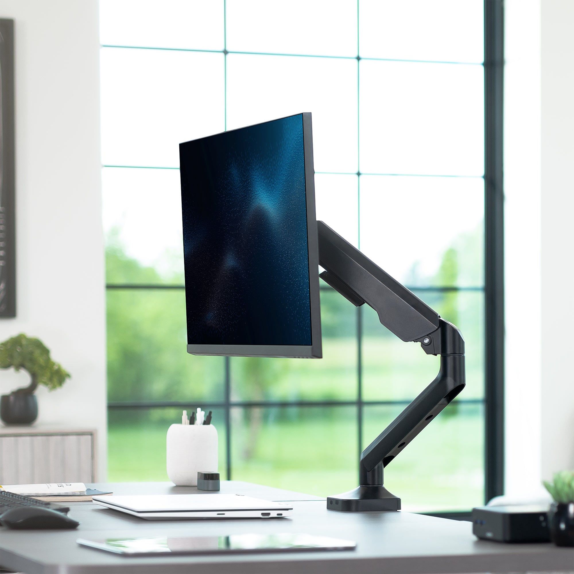 Monitor on a adjustable arm on a desk with a blurred window background