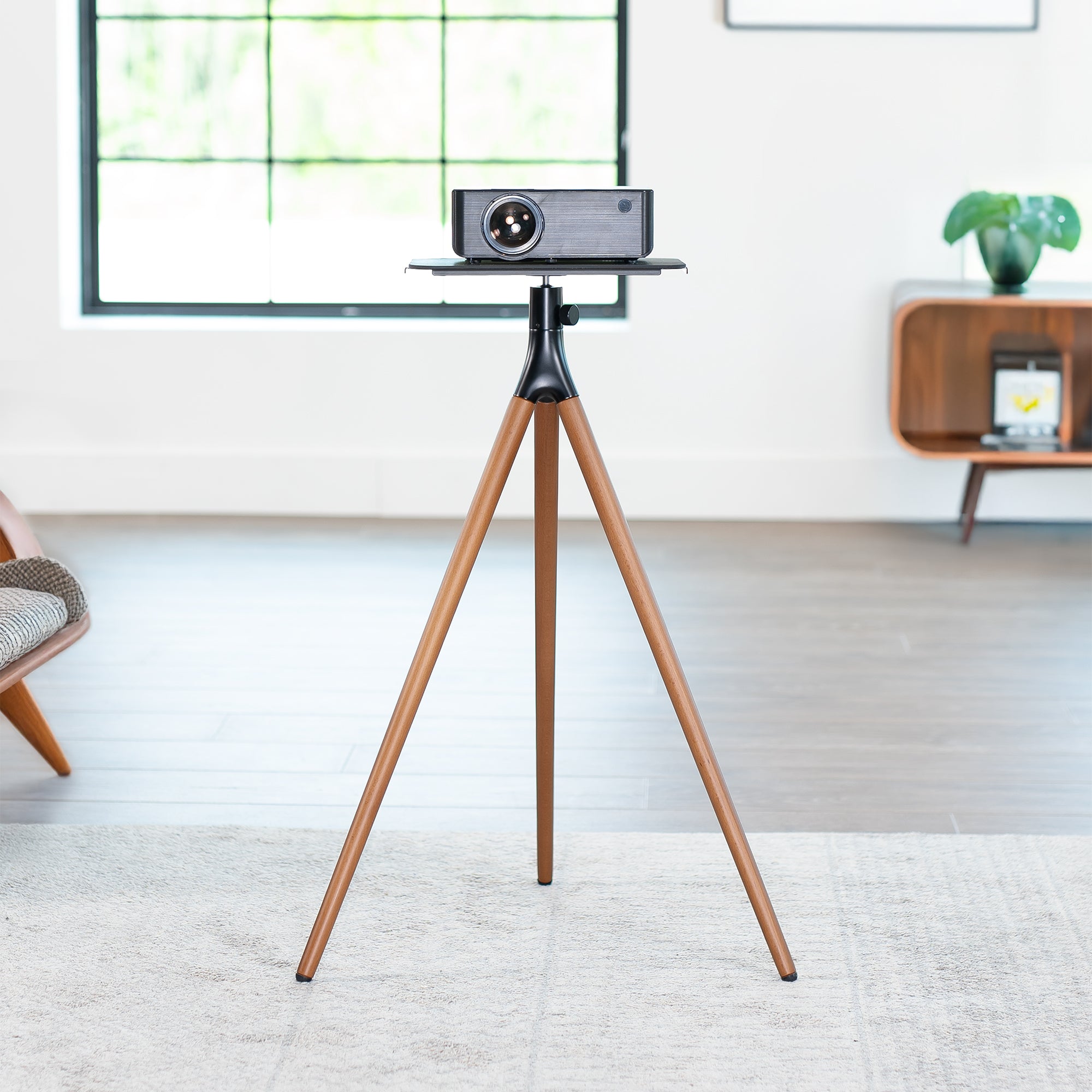 Projector on a wooden tripod stand in a room with a window and furniture.