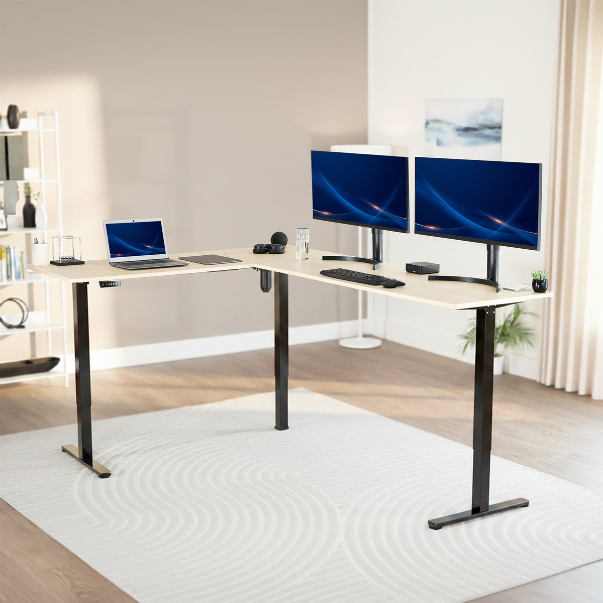 Modern office setup with a standing l-shaped desk, laptop, and two monitors in a bright room.