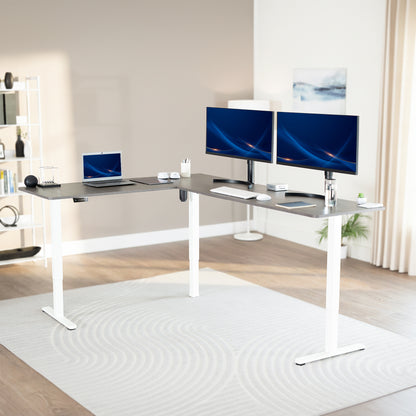 Modern office setup with a standing l-shaped desk, laptop, and two monitors in a bright room.
