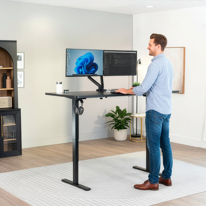 Man using a standing desk with dual monitors in a home office setting.