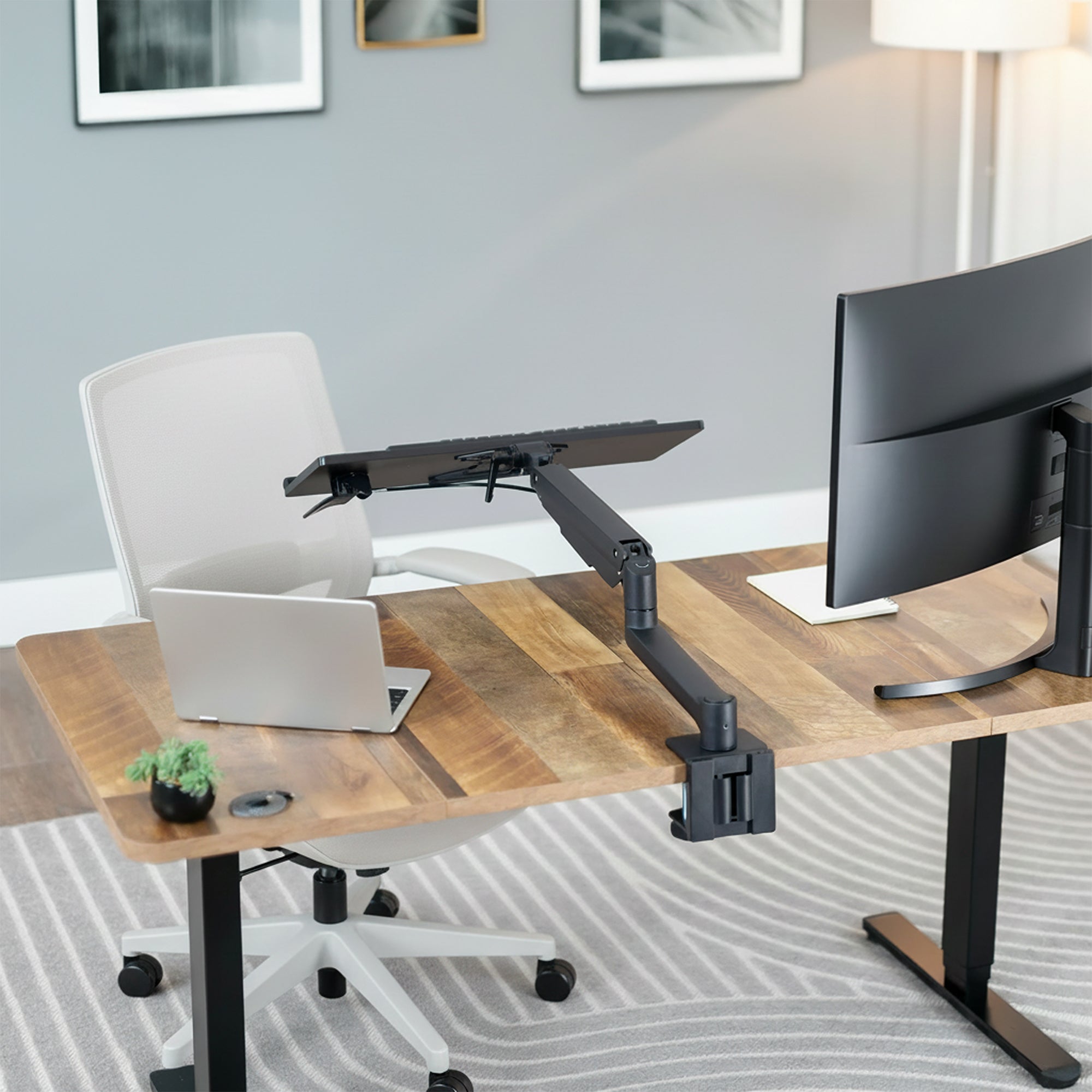 Modern office setup with a adjustable standing desk, laptop, monitor, and keyboard on an adjustable keyboard mount.