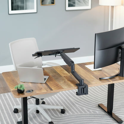 Modern office setup with a adjustable standing desk, laptop, monitor, and keyboard on an adjustable keyboard mount.