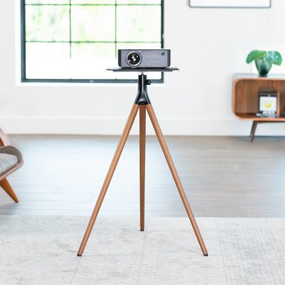 Projector on a wooden tripod stand in a room with a window and furniture.