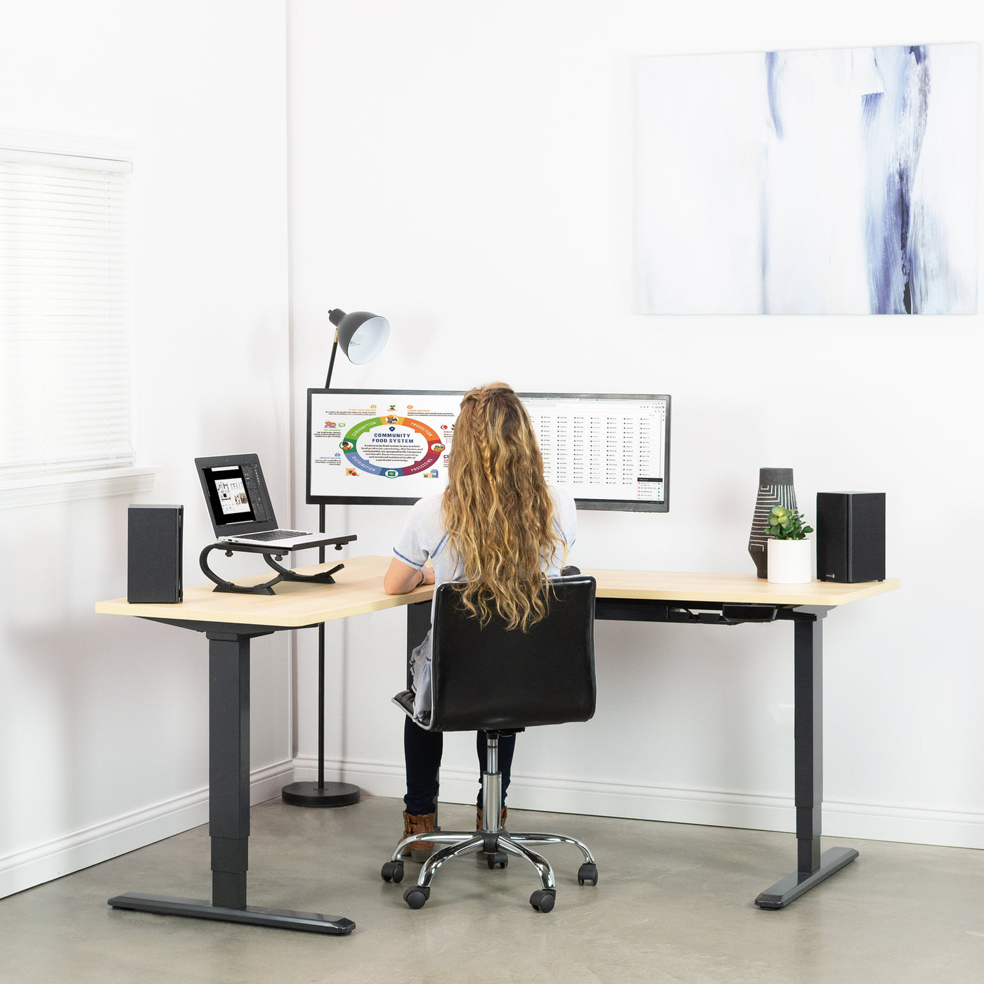 A woman working from an ergonomic sit to stand L-shaped desk.
