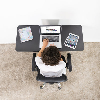 A woman using a folding shelf in a small at-home office as a workspace.